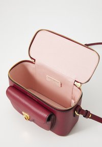 Small burgundy leather handbag with gold zipper and clasp, pink fabric interior, and adjustable shoulder strap.