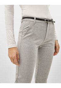 Pantalons tailleurs gris avec une finition texturée, dotés de poches latérales, d'une ceinture noire avec une boucle en argent, et d'un design ajusté.