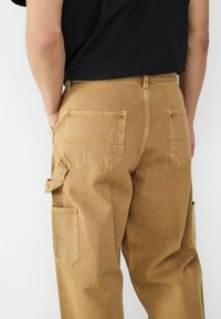 Khaki Cargo-Hosen mit entspannter Passform, ausgestattet mit mehreren Taschen, verstärkten Nähten und einem strukturierten Baumwollstoff.