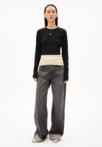 Schwarzes Langarmoberteil mit einem cremefarbenen gerippten Saum, kombiniert mit weiten grauen Jeans aus Denim und einzigartigen, silberakzentuierten Schuhen. Minimalistisches Design.