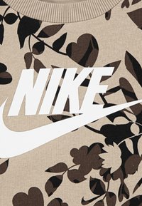 Brun genser med mørkt blomstermønster og stor hvit "NIKE"-logo. Har ribbestrikket rund hals og myk strikket tekstur.