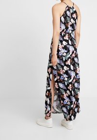 Maxi šaty s černým pozadím, zdobené barevnými květinovými a listovými vzory. Mají halter krk, otevřená záda a boční rozparky.