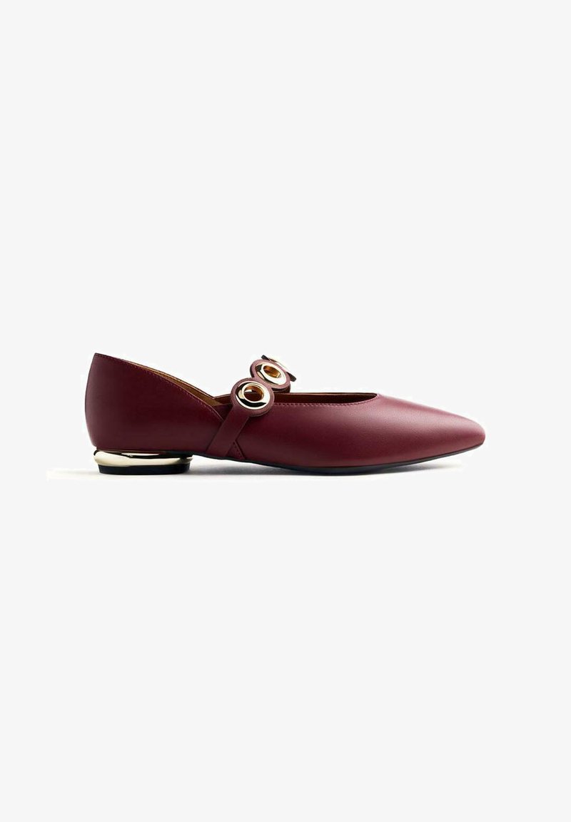 Chaussure plate en cuir bordeaux avec un bout pointu, deux accents ronds dorés sur la sangle et un petit talon doré. Texture lisse et design épuré.