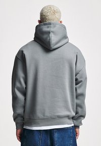 Felpa grigia con cappuccio in tessuto morbido, dotata di un cappuccio ampio, polsini e orlo a coste. Indossata con jeans in denim blu.