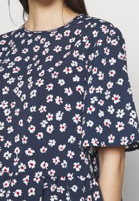 Floral dress featuring navy fabric with white and red flower patterns, round neckline, short sleeves, and a flared hem.