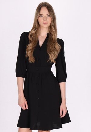 Schwarzes Hemdkleid mit taillierter Taille, dreiviertel Ärmeln und schwingendem Rock. Aus leichtem Stoff mit glatter Textur gefertigt.