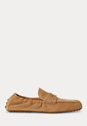 Mocassin en daim marron clair avec avant cousu, dos élastique et semelle en caoutchouc cloutée, vu de côté sur un fond uni.