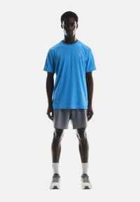T-shirt de sport bleu à manches courtes et encolure ronde, associé à un short gris clair. Présente un détail de logo sur le t-shirt.