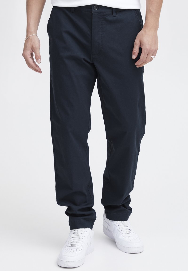 Mørkeblå bomullsbukser med rett snitt, med frontknapplukking og sidelommer, kombinert med hvite sneakers.