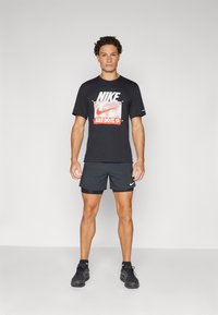 Svart Nike T-skjorte med grafisk logo og "JUST DO IT." kombinert med svarte shorts og svarte treningssko. Renslig design, uformell passform.