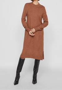 Vestito maglione marrone a maglia con maniche lunghe, polsini a coste e scollo rotondo. Presenta spaccature laterali sull'orlo e una texture morbida.