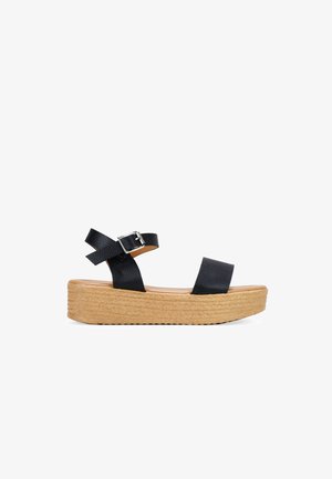 Sandales à talon en wedge noires avec des brides texturées et une boucle. Semelle tissée naturelle avec une légère élévation, semelle intérieure lisse et design minimaliste.