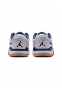 Vita sneakers med grå mocka och marinblå detaljer, med en gummisula och Jumpman-logotyp på hälen. Rund tådesign och vadderad krage.