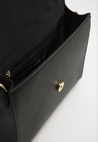 Černá kožená kabelka s klopovým zapínáním, zlatým kováním a vnitřní kapsou na zip. Podšívka z černé látky s vnitřní značkou značky.