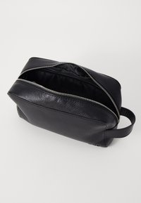 Black leather toiletry bag with a textured finish, zip closure, and a side handle. Interior is lined in black fabric.