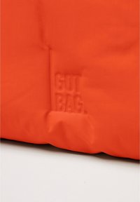 Borsa in tessuto arancione con superficie testurizzata. Presenta il marchio in rilievo "GOT BAG" su un lato. Design semplice, materiale leggero.