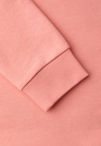 Tissu de sweat-shirt rose clair présentant un poignet côtelé. Le matériau a une texture lisse avec une finition uniforme et aucun motif visible.