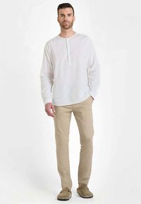 Witte linnen blouse met lange mouwen en een korte knoopsluiting, gecombineerd met licht beige broek en bruine suède schoenen. Eenvoudige, ontspannen pasvorm.