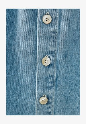 Lichtblau denim stof met een verticale rij van vier ronde, parelachtige knopen, met een gestructureerd oppervlak en gestikte details.