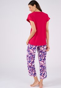 Top corto de manga corta rojo combinado con pantalones morados que presentan un patrón de hojas en blanco y rosa. Tela suave con un ajuste relajado.