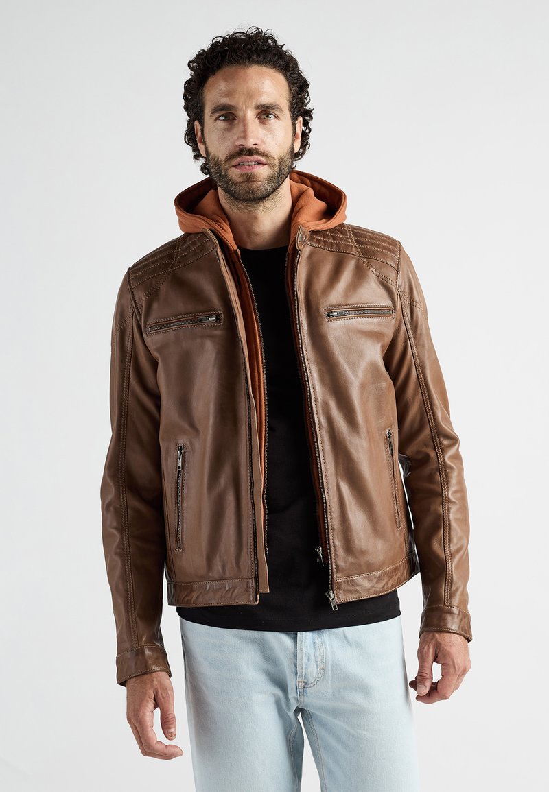 Bruine leren jas met een oranje capuchon, voorzien van diagonale stiksels, voorzakken met rits en een slim-fit design. Draag over een zwart shirt.