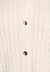 Valget värvitud soonikkoes kardigan, mille keskel on kolm kuldset nööpi sulgemiseks.