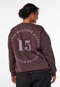 Brown pullover sweatshirt with oversized fit, featuring a large graphic design on the back, including the number “15” and text in white.