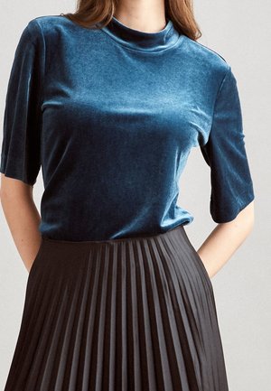 Velvet teal top with a high neck and short sleeves paired with a black pleated skirt, showcasing smooth texture and elegant design.