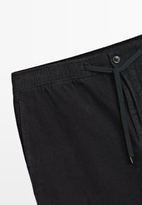 Zwarte corduroybroek met een gestructureerd oppervlak, voorzien van een elastische tailleband, knoopsluiting en trekkoord voor een verstelbare pasvorm.