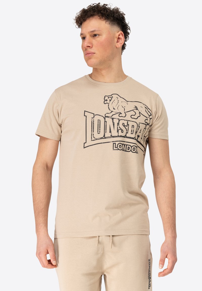 Beige kokvilnas t-krekls ar īsām piedurknēm, ar melnu lauvu grafiku un "Lonsdale London" tekstu, apaļa dekoltē un mīksta tekstūra.