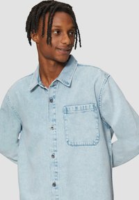 Lichtblauwe denim shirt met een button-up voorkant, een puntige kraag en een enkele borstzak. De stof heeft een zachte textuur.