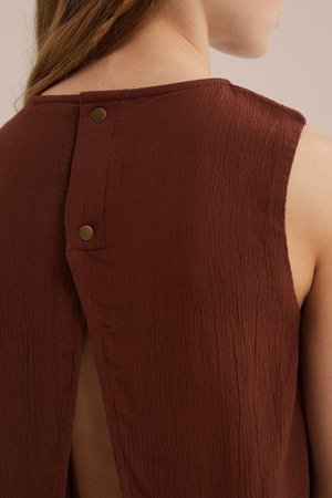 Krupni plan osobe koja nosi smeđi top bez rukava s teksturom i dva metalna kopčasta gumba na gornjem dijelu leđa.