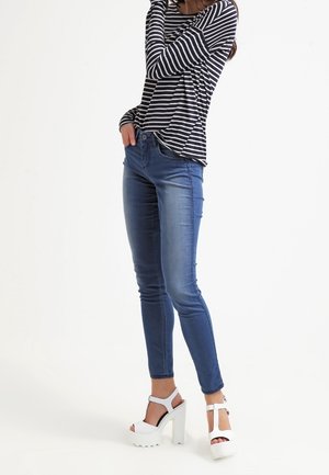 Haut à manches longues rayé en noir et blanc, associé à un jeans skinny bleu et des sandales blanches à plateforme avec des talons épais.