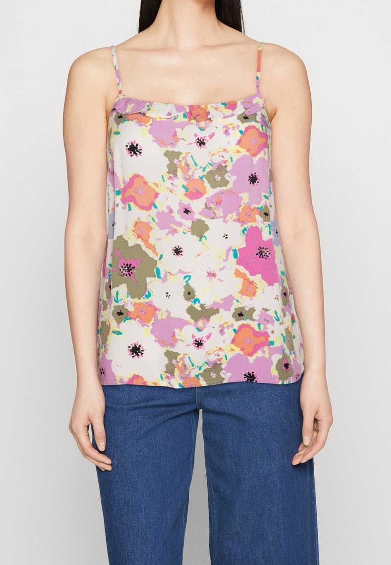 Femme portant un haut sans manches à motifs floraux rose, violet, orange et vert, associé à un pantalon en denim bleu.