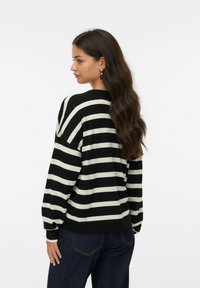 Pull rayé noir et crème avec une coupe ample, des poignets côtelés et un col rond, assorti à un jean en denim foncé.