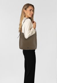 Braune Leder-Tote mit glatter Oberfläche, vertikaler Form und verstellbaren Schulterriemen, vor einem neutralen Hintergrund präsentiert.