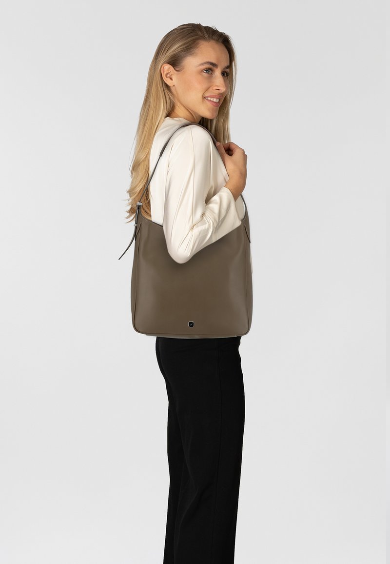 Braune Leder-Tote mit glatter Oberfläche, vertikaler Form und verstellbaren Schulterriemen, vor einem neutralen Hintergrund präsentiert.