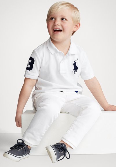 Biela polokošeľa s námorníckymi akcentmi, s vyšívaným logom a číslom 3. Kombinovaná s bielymi nohavicami a sivými teniskami s bielymi podrážkami.