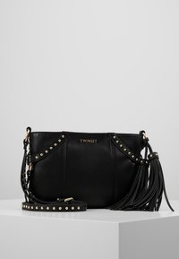 Borsa in pelle nera con accenti borchiati, una tracolla con frange e un logo dorato. Presenta un design strutturato e una tracolla regolabile.