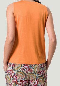 Orange ærmeløs top lavet af blødt stof, parret med mønstrede bukser med flerfarvede blomsterdesigns på en cremefarvet baggrund.