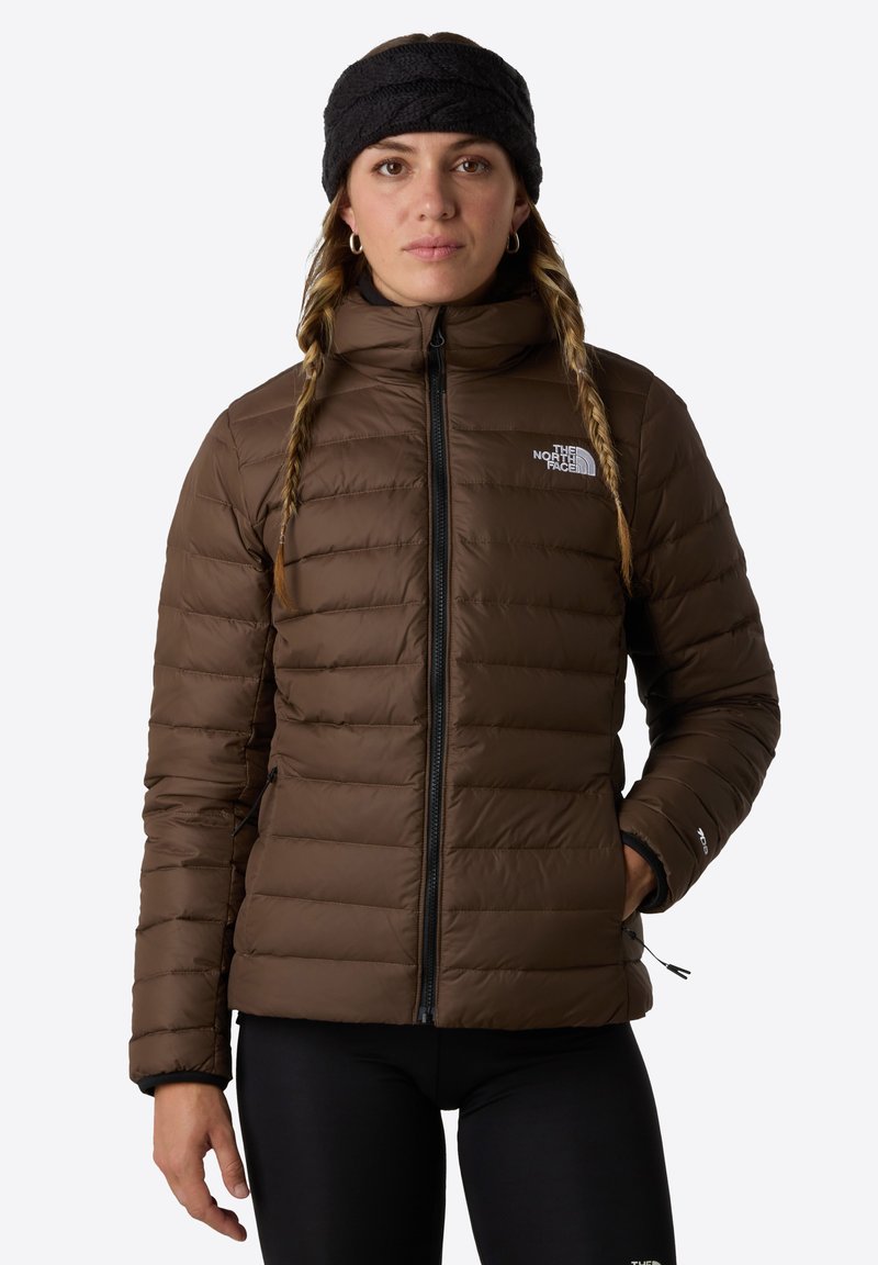 Brązowa kurtka puchowa z pionowymi szwami, wysokim kołnierzem i zapinanymi na zamek kieszeniami. Noszona z czarną opaską na włosy, w połączeniu z czarnymi leginsami.