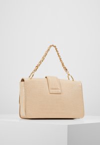 Beige fusk-krokodil handväska med en texturerad yta, rektangulär form och ett guldkedjestraps. Har en klaffstängning och släta kanter.