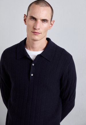 Navy knitted polo sweater with a textured pattern, button placket, and a classic pointed collar; features long sleeves and a relaxed fit.