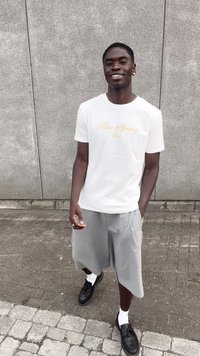 White short-sleeve t-shirt with "Palm Spring" in gold lettering, paired with light gray shorts and black loafers over white socks.