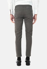 Chinos slim fit grigio scuro in cotone misto, con una texture liscia. Presentano due tasche posteriori e gambe affusolate. Indossati con scarpe nere.