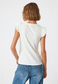 Witte ribbel top met korte ruches mouwen en een ronde halslijn, gecombineerd met blauwe denimjeans, waardoor een getailleerde silhouette wordt benadrukt.