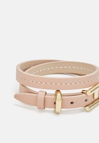 Gaiši bēša dubultā ādas josta ar baltu šuvumu un spīdīgu zelta taisnstūra sprādzi, salocīta un novietota uz balta fona.