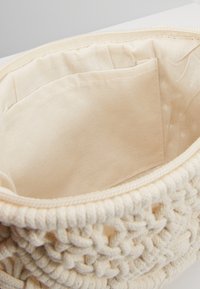 Kremowa bawełniana torba z plecioną powłoką, z gładkim wnętrzem i małą kieszenią; zapięcie to zamek błyskawiczny na górze.