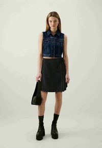 Top cropped de ganga, saia de ganga escura e botas plataforma pretas. A modelo segura uma bolsa preta. Design simples com pouca decoração.