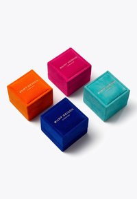 Quatre boîtes à bijoux en velours, carrées, de couleur orange, rose, bleu et teal, chacune ornée de texte en or inscrivant "Kurt Geiger London."